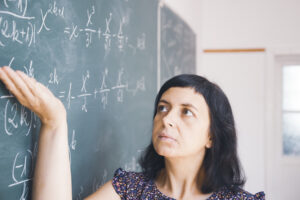 Female student or teacher in the classroom writing on chalkboard mathematical equations